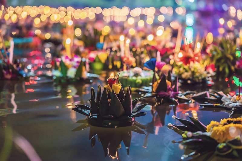 The Luminous Krathong decorated with flowers and candles floating on the water.